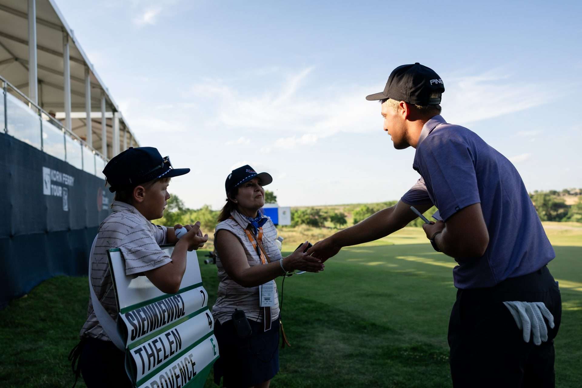 Kid holding a stats sign standing on the side of the golf course as a tournament volunteer